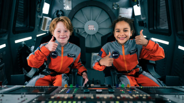 Chłopiec i dziewczynka siedzą w statku kosmicznym w uniformach astronautów.