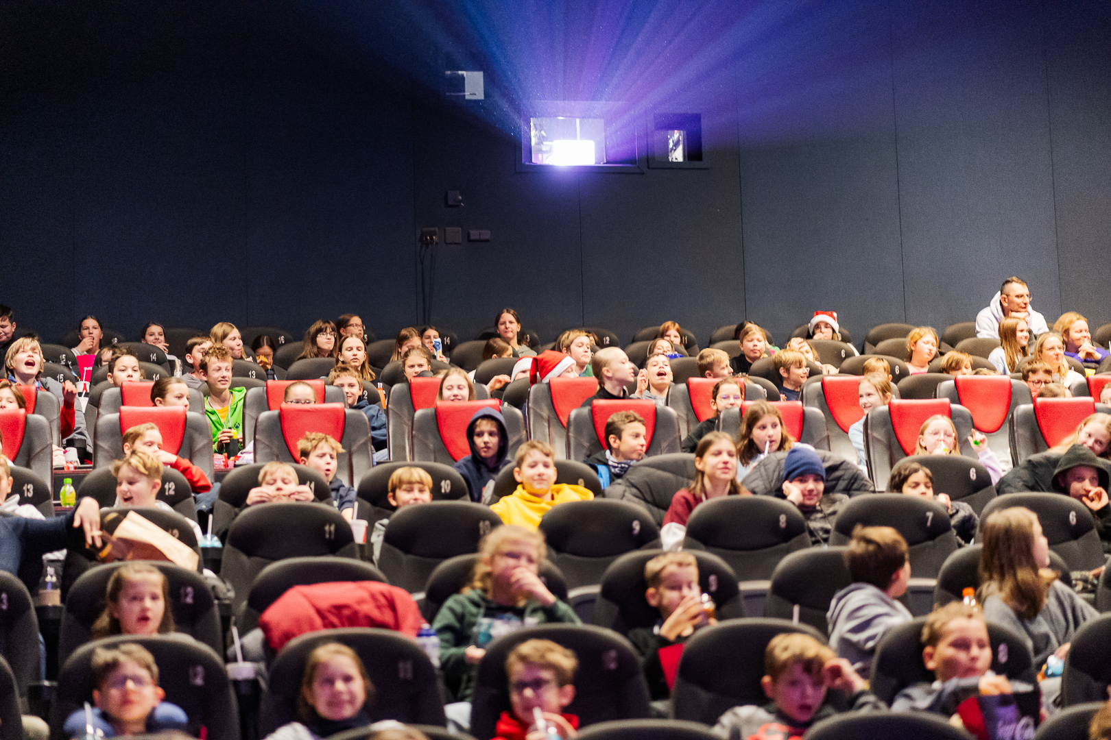 Roześmiane dzieci siedzące w fotelach na sali filmowej.