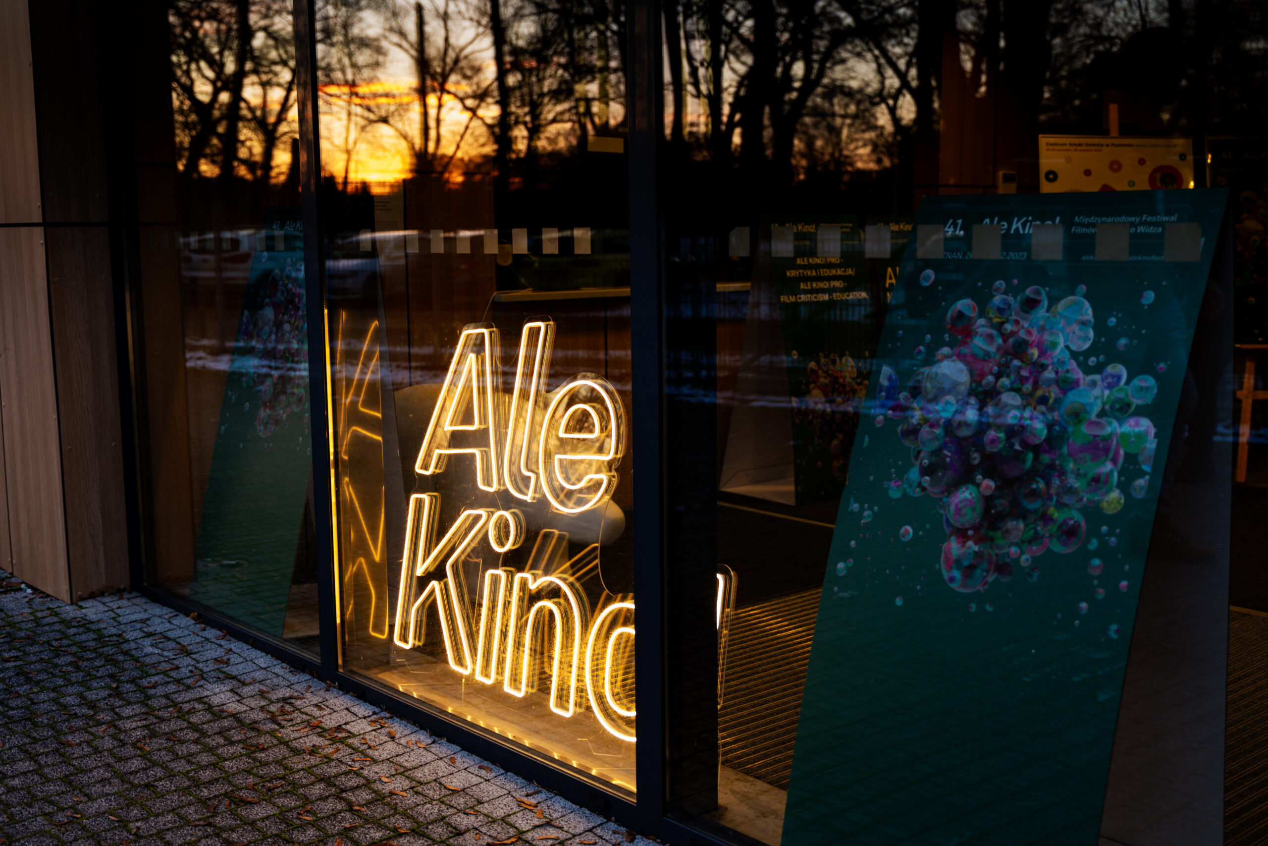 Rozświetlony neon z napisem Ale Kino! widoczny za szybą.