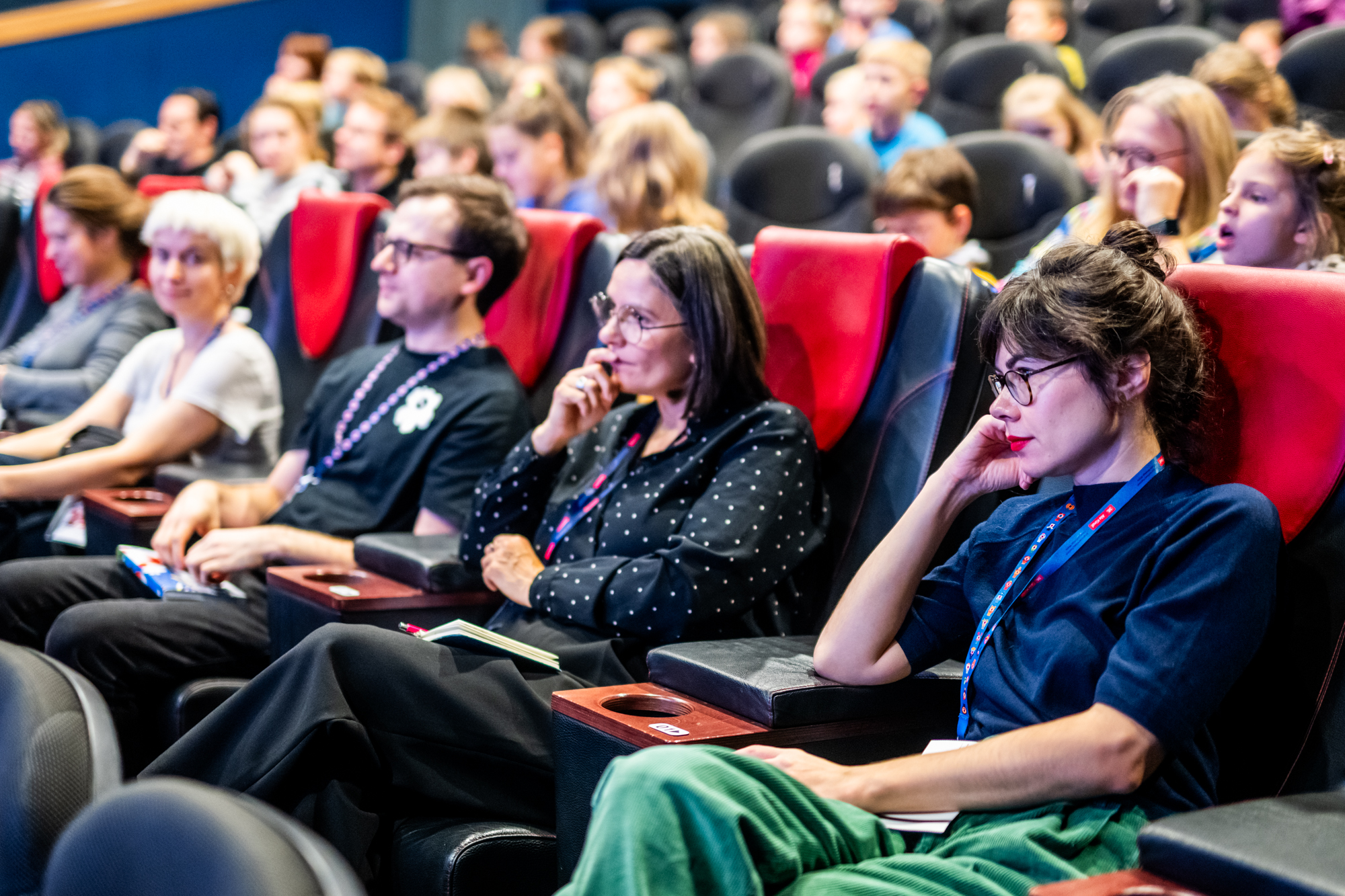 grupa osób siedzących w fotelach na sali kinowej, z zaangażowaniem oglądają film