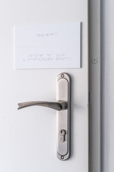 Fragment drzwi z klamką. Nad klamką tabliczki z alfabetem Braille'a