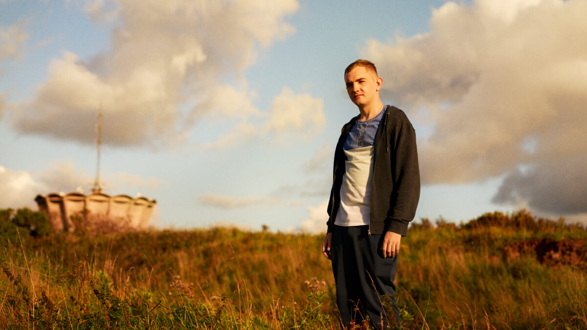 chłopiec ubrany w czarną kurtkę stoi pośród pola