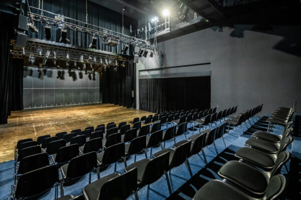Pusta sala teatralna z długimi rzędami czarnych krzeseł.