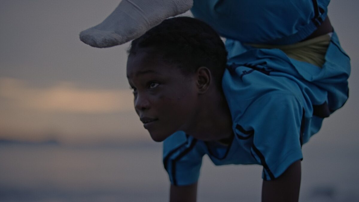 Ciemnoskóra dziewczyna stoi na rękach i ma nogi przy głowie