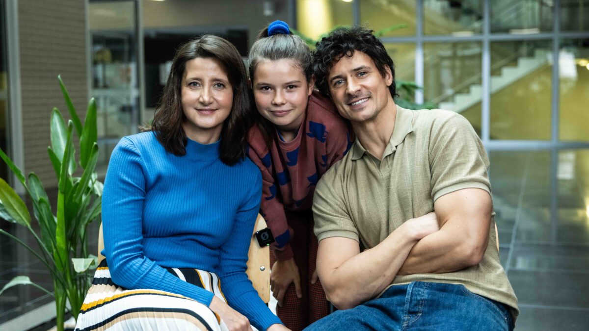 Kobieta, dziewczynka i mężczyzna siedzą razem, przytuleni, uśmiechnięci do kamery