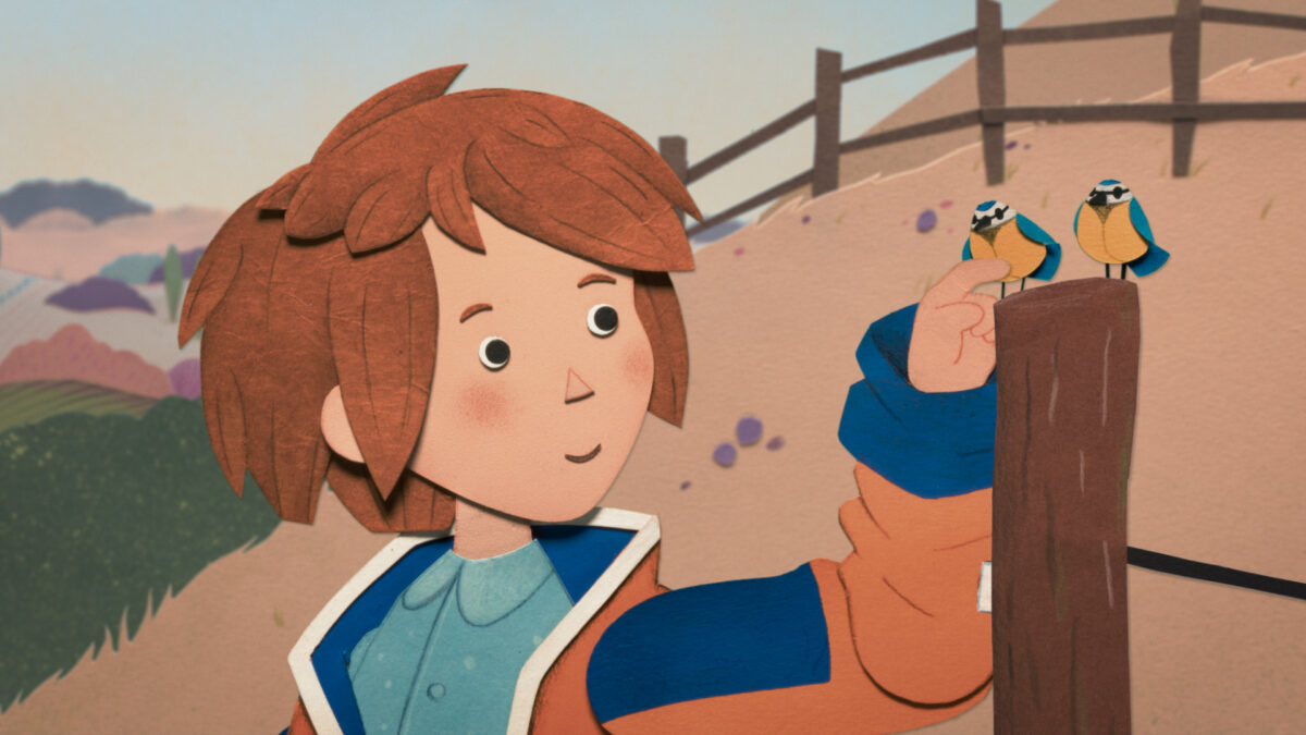 Chłopiec o rudych włosach delikatnie sadza ptaszka na palcu