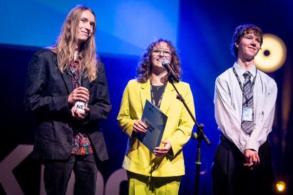 mężczyzna, kobieta i mężczyzna mówią do mikrofonu na scenie