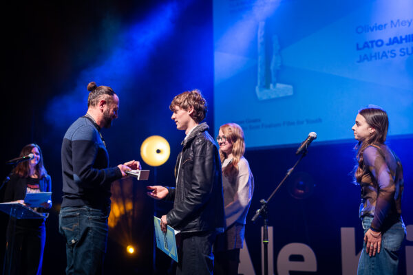 mężczyzna odbiera nagrodę na scenie od trójki nastolatków