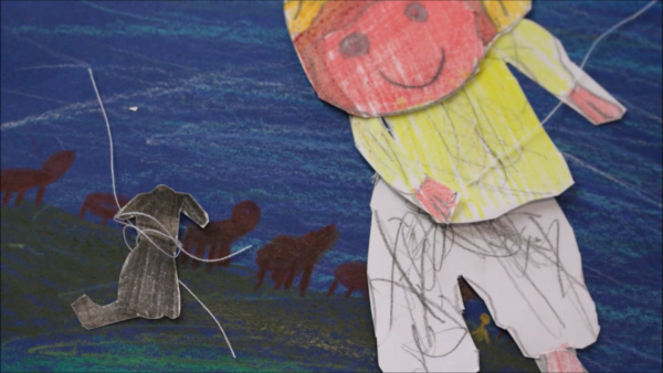 Kadr z filmu animowanego, papierowa postać dziecka stojąca na niebieskim tle obok małego rysunkowego psa, a w tle widać sylwetki zwierząt przypominających konie lub krowy.