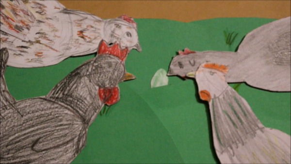 Kadr z filmu animowanego, kilka papierowych kur stoi na zielonej łące i patrzy na mały zielony kamień pośrodku.