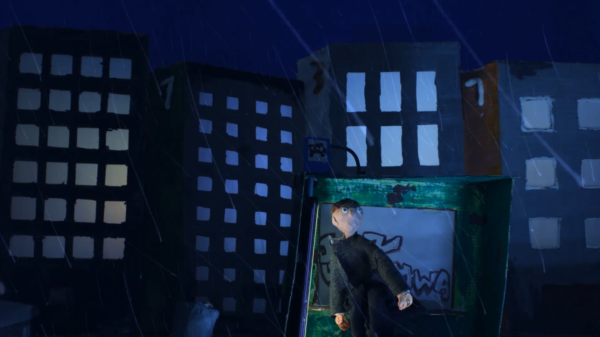 Kadr z filmu animowanego, nocna scena miasta podczas deszczu, postać stoi w oświetlonej przestrzeni na tle budynków.