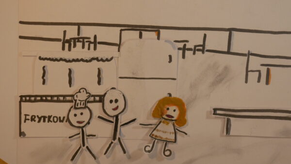 Kadr z filmu animowanego, rysunkowe postacie stoją w kuchni, obok widoczny jest napis i elementy wyposażenia wnętrza.