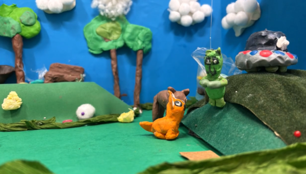 Kadr z filmu animowanego, plastelinowe postacie i zwierzęta znajdują się na zielonym wzgórzu z drzewami i chmurami.