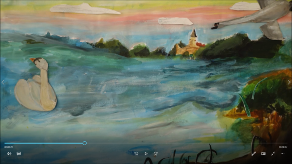 Kadr z filmu animowanego, papierowy łabędź pływa po jeziorze, a w oddali widać wieś z kościołem i drzewa.