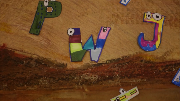 Kadr z filmu animowanego, kolorowe literki z oczami układają się na tle malarskiego krajobrazu w odcieniach brązu.