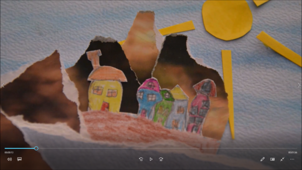 Kadr z filmu animowanego, kolorowe papierowe domki stoją obok siebie pod żółtym słońcem na tle porwanych fragmentów papieru tworzących krajobraz.
