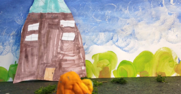 Kadr z filmu animowanego przedstawia namalowany budynek na tle nieba oraz niewielką postać znajdującą się przed nim.