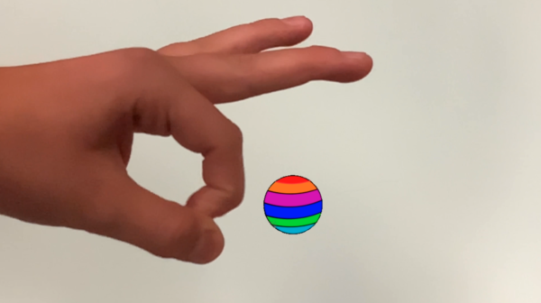Kadr z filmu animowanego przedstawia dłoń trzymającą małą, kolorową kulkę na jasnym tle.