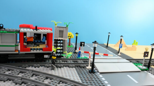 Kadr z filmu animowanego, czerwono-szary pociąg z klocków LEGO przejeżdża przez przejazd kolejowy z opuszczonym szlabanem wśród ulicznych latarni.