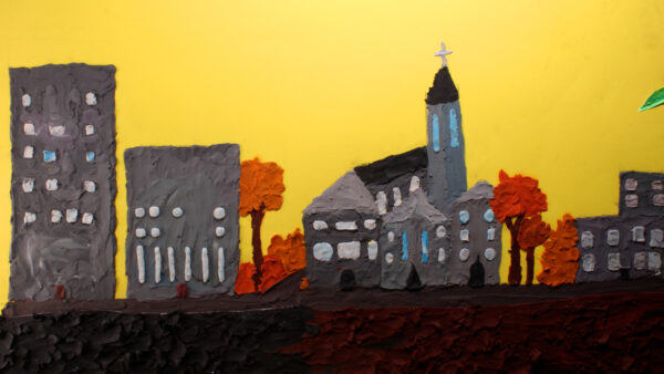 Kadr z filmu animowanego, makieta miasta zbudowana z plasteliny przedstawia budynki, kościół oraz drzewa na tle żółtego nieba.