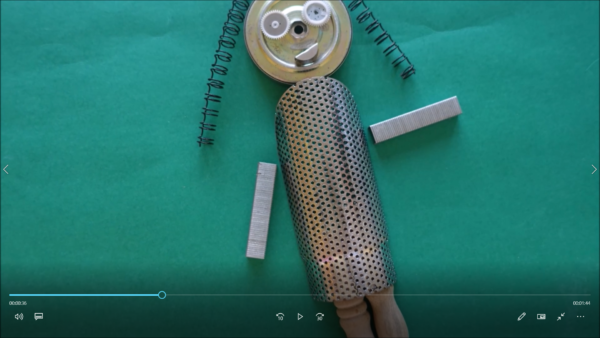 Kadr z filmu animowanego, postać robota zbudowana z metalowych części i sprężyn leży na zielonym tle przypominającym planszę.