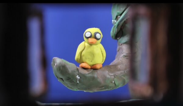 Kadr z filmu animowanego ukazuje małą figurkę żółtego ptaka stojącą na dłoni większej postaci.