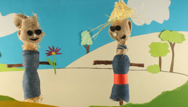 Kadr z filmu animowanego, dwie kukiełki przypominające strachy na wróble stoją na polu obok stylizowanego kwiatka i drzew.