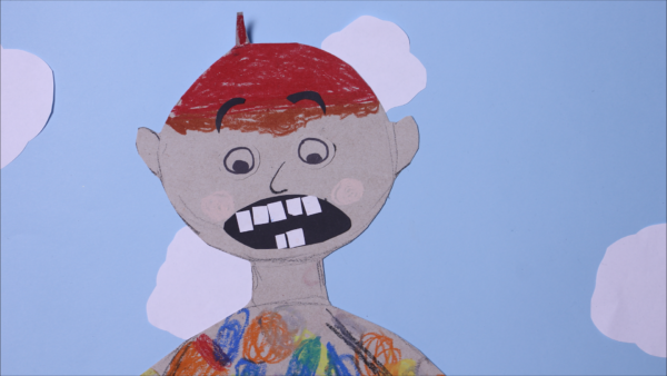 Kadr z filmu animowanego, papierowa twarz dziecka z szeroko otwartymi ustami i widocznymi zębami znajduje się na tle nieba z białymi chmurami.