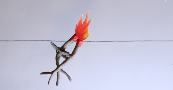 Kadr z filmu animowanego, niewielkie ognisko płonie na skrzyżowanych gałęziach na jasnym, pustym tle.