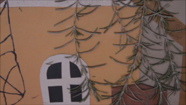 Kadr z filmu animowanego, niewielki domek z oknem otoczony jest gałązkami roślin na tle ciepłego, pomarańczowego tła.