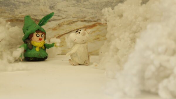 Kadr z filmu animowanego, plastelinowa postać w zielonym stroju stoi obok białego zwierzęcia na tle jasnej przestrzeni z miękkimi, chmurowymi formami.