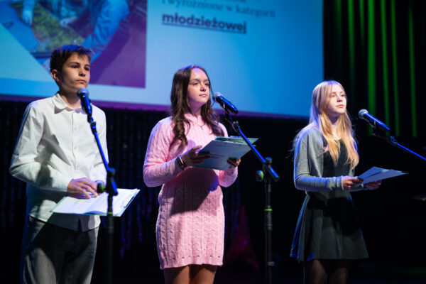 nastolatek i dwie nastolatki stoją na scenie i mówią do mikrofonu