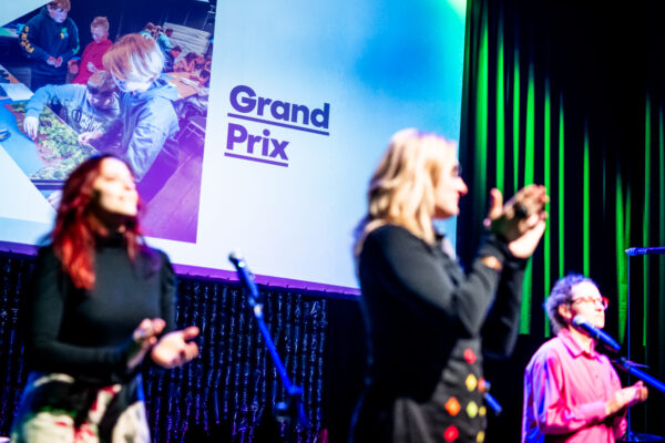 Trzy kobiet na scenie, za nimi na ekranie napis na slajdzie Grand Prix